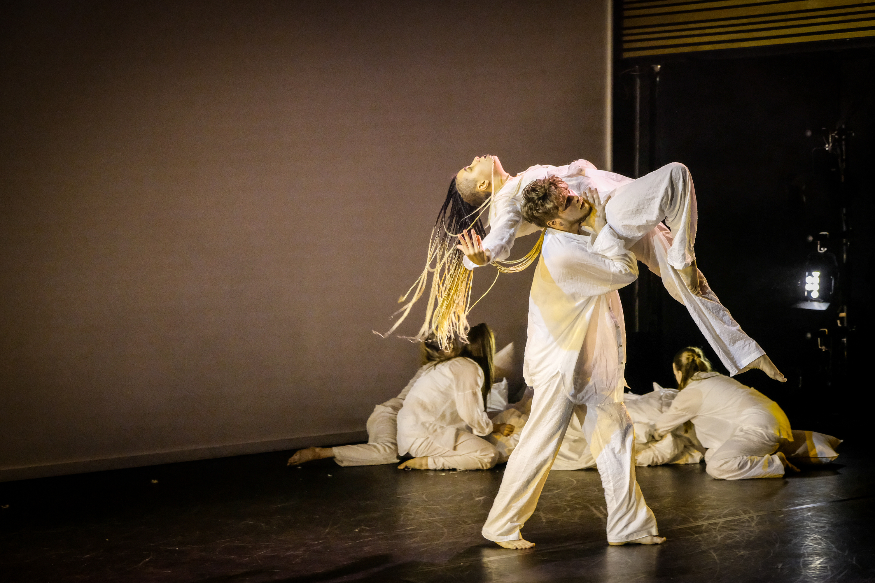One dancer lifts another on a dimly lit stage with dramatic lighting