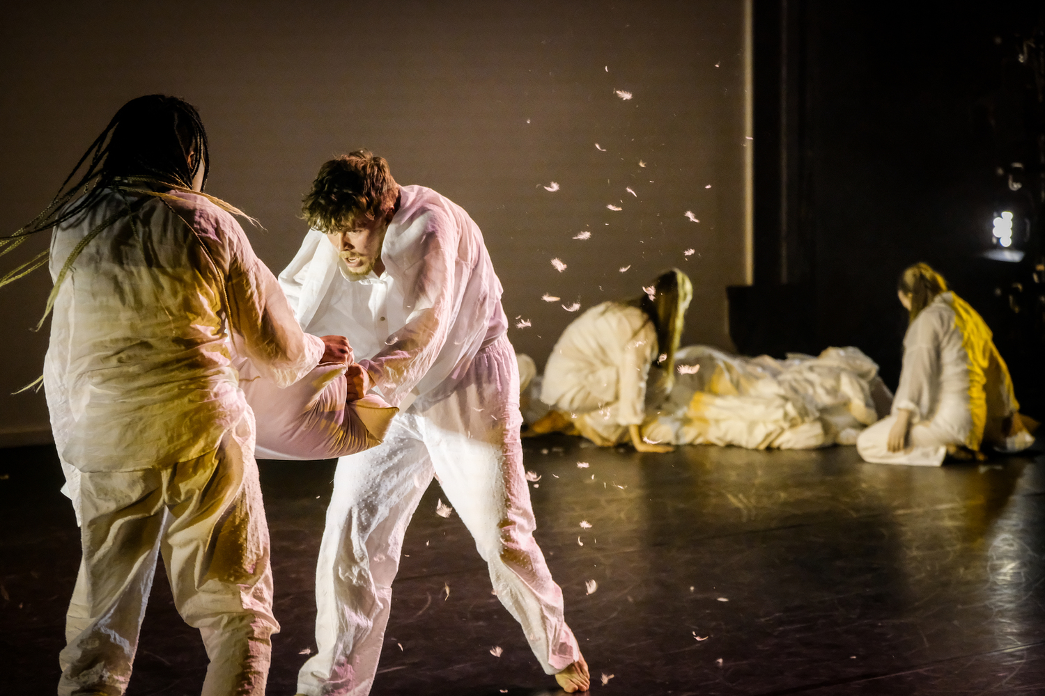 Two dancers hit each other with pillows, leaving feathers trailing across the stage
