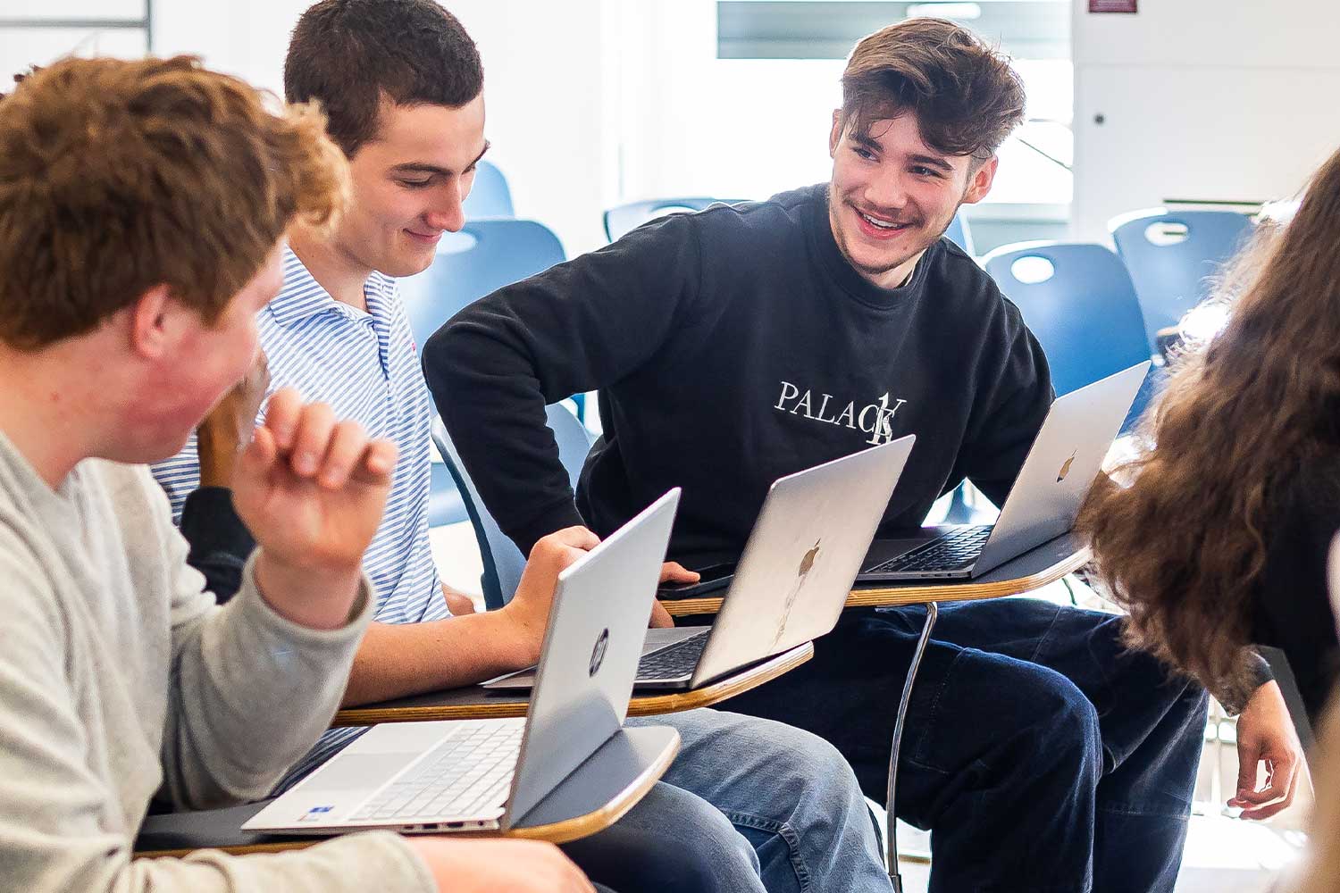 Three students sit with laptops in a lecture