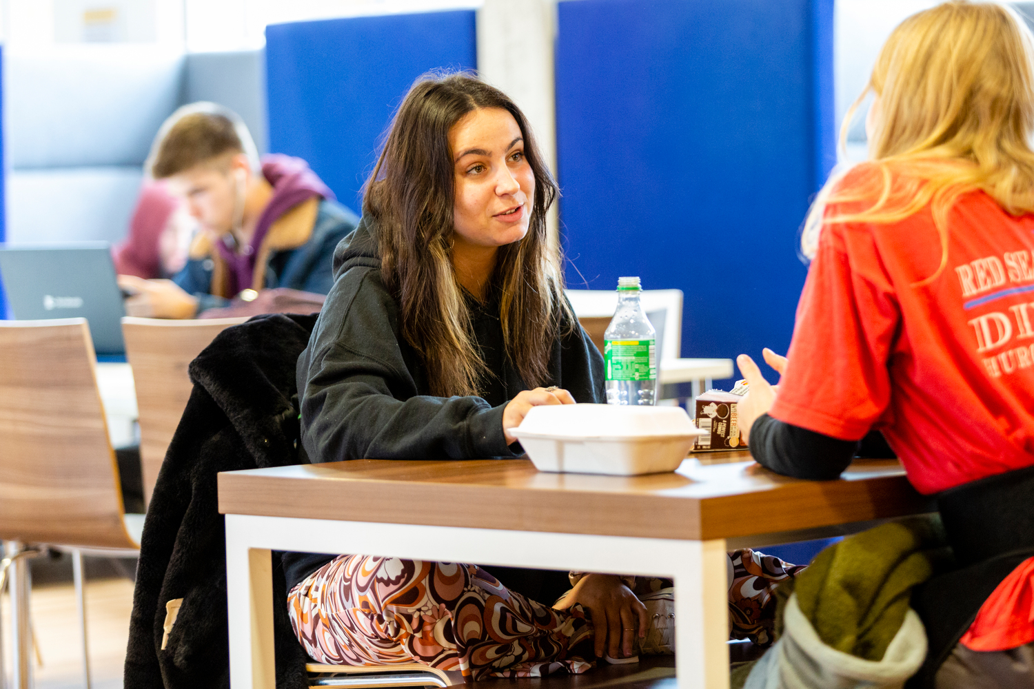 Two students sit at a table with takeaway food