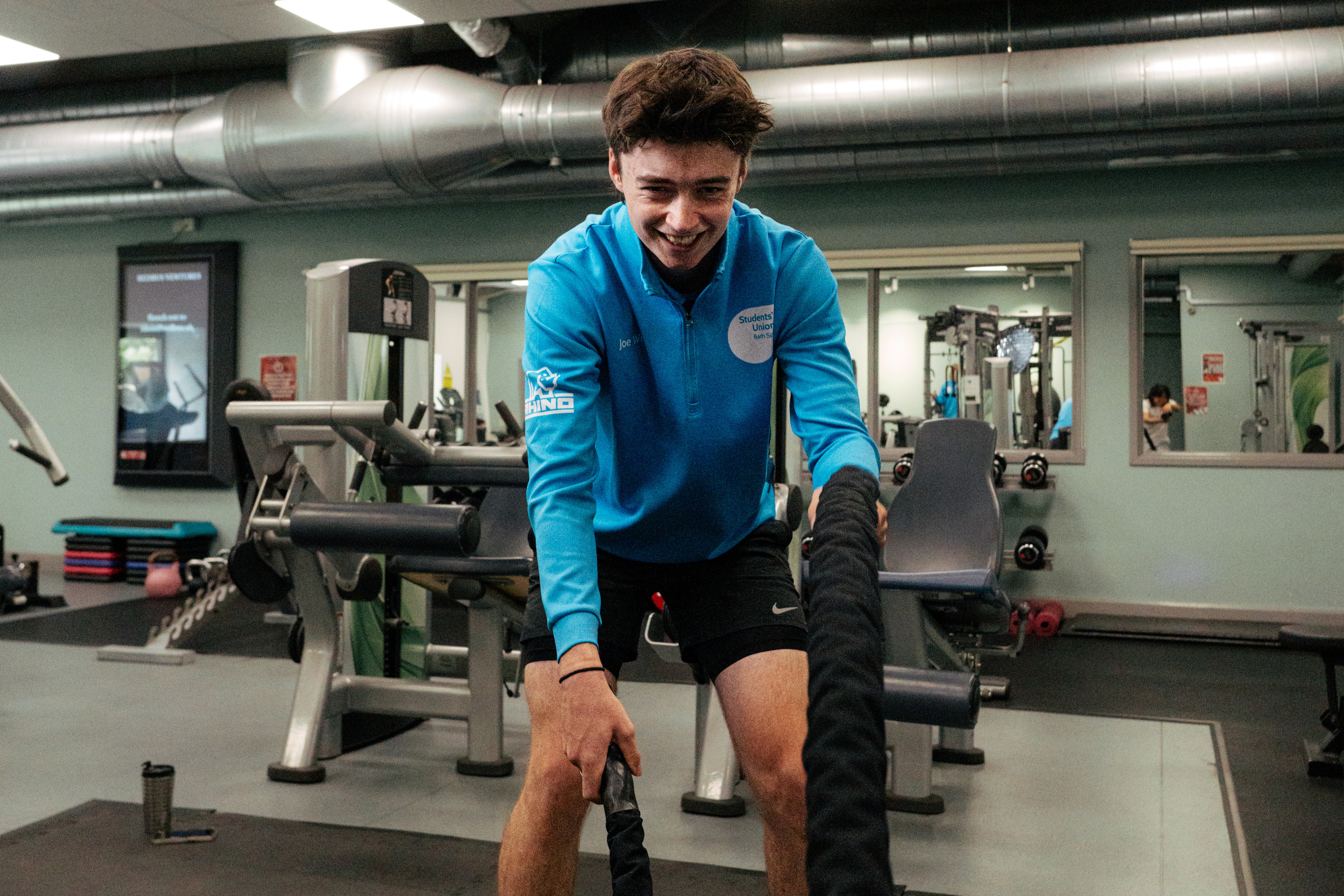 A person working out in a gym while wearing a blue branded SU hoodie