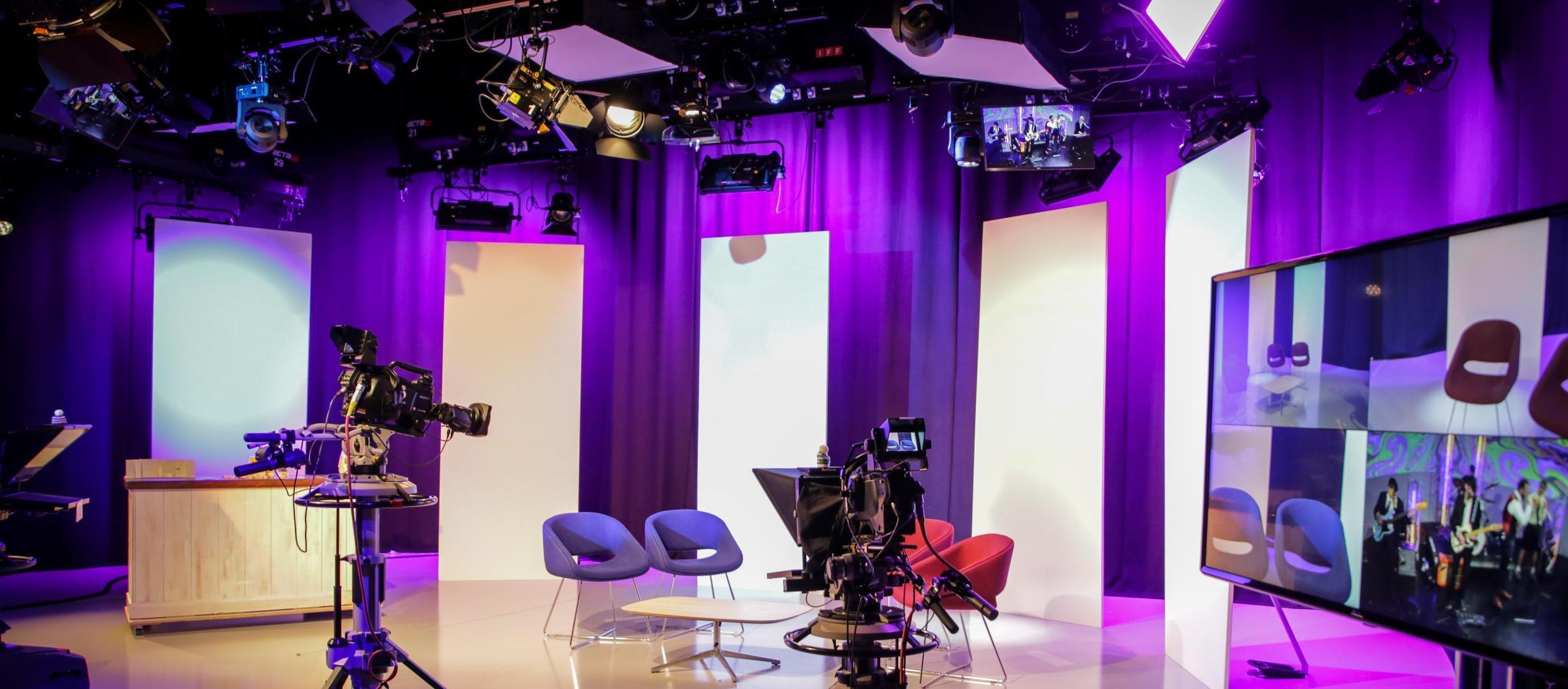 Purple lighting in a TV studio filled with equipment and a set