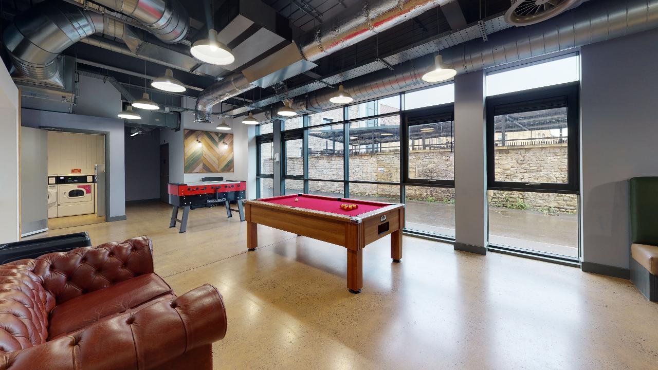 A large communal seating area with pool tables and large glass windows