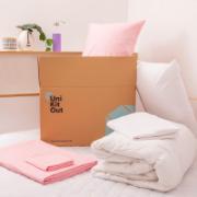 A cardboard box next to pink bedsheets and a duvet
