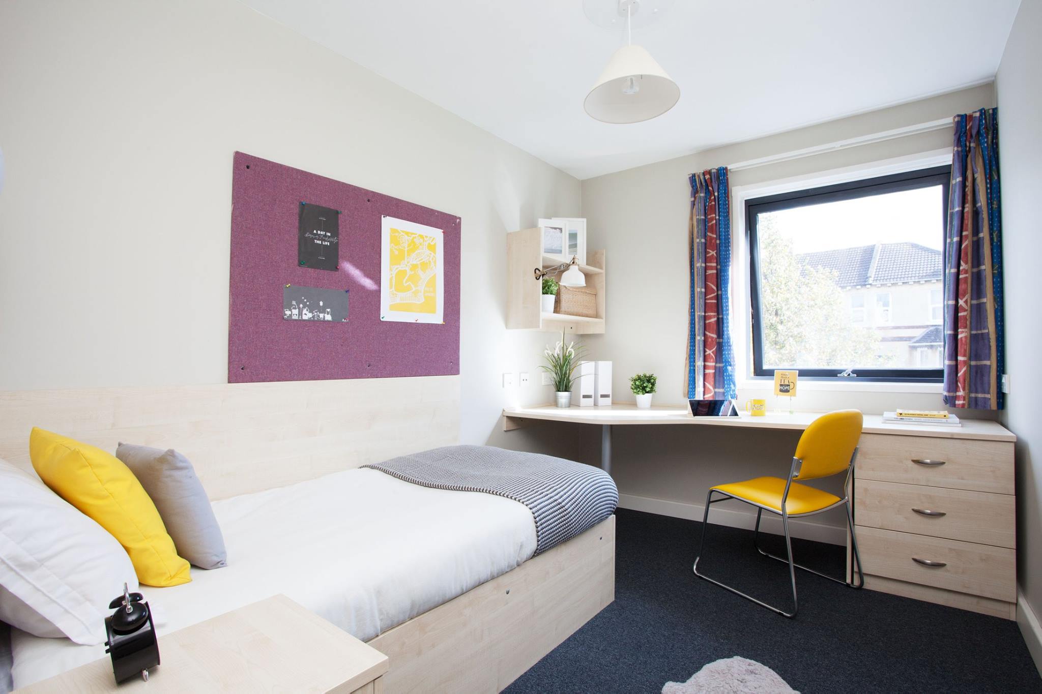 A student bedroom with a bed, desk, chair and noticeboard