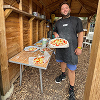 A student serving pizzas in a wooden hut.