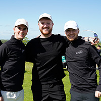 Three students in caps stand in a field.