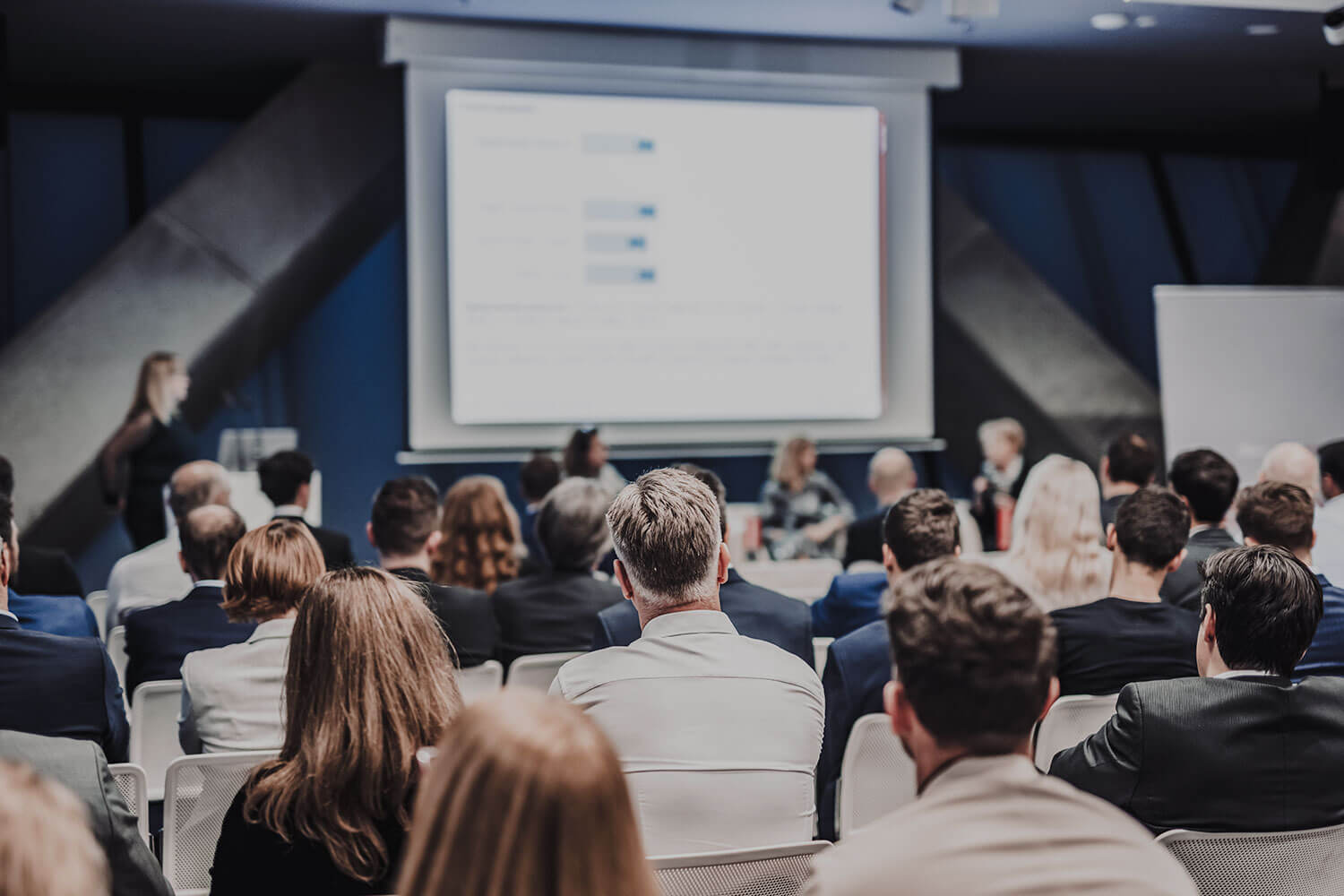 A audience watches a speaker at a conference