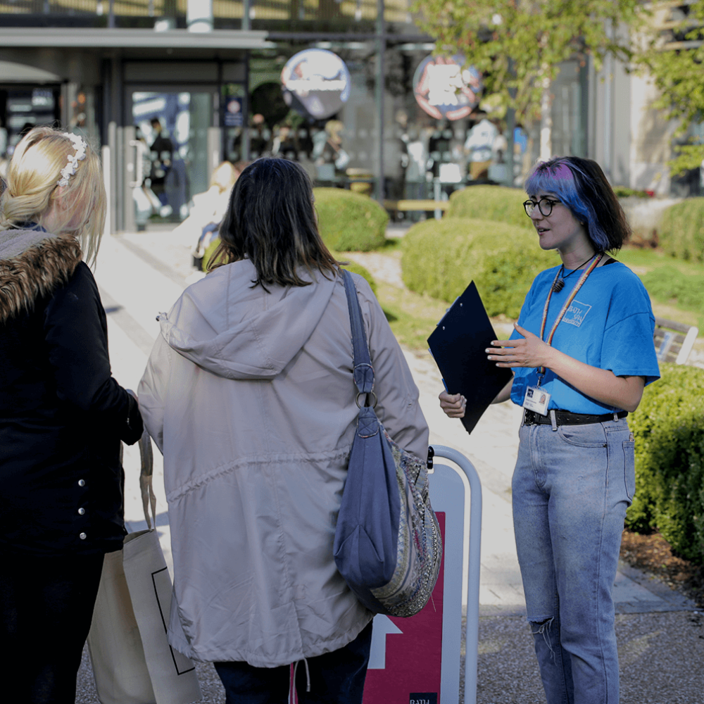 a student ambassador is holding the prospectus and talking to a family at an open day for bath spa university