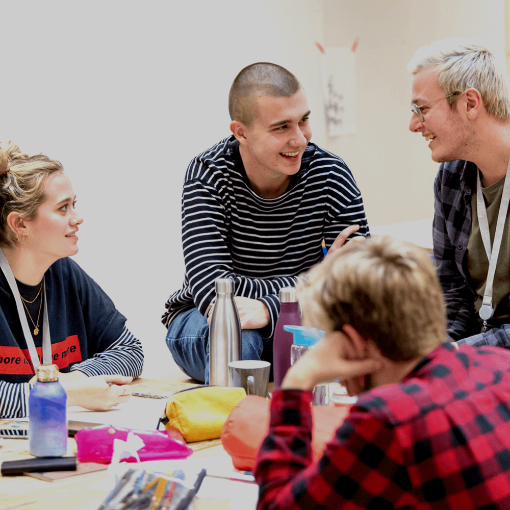 four students sit around a table smiling and talking to each other