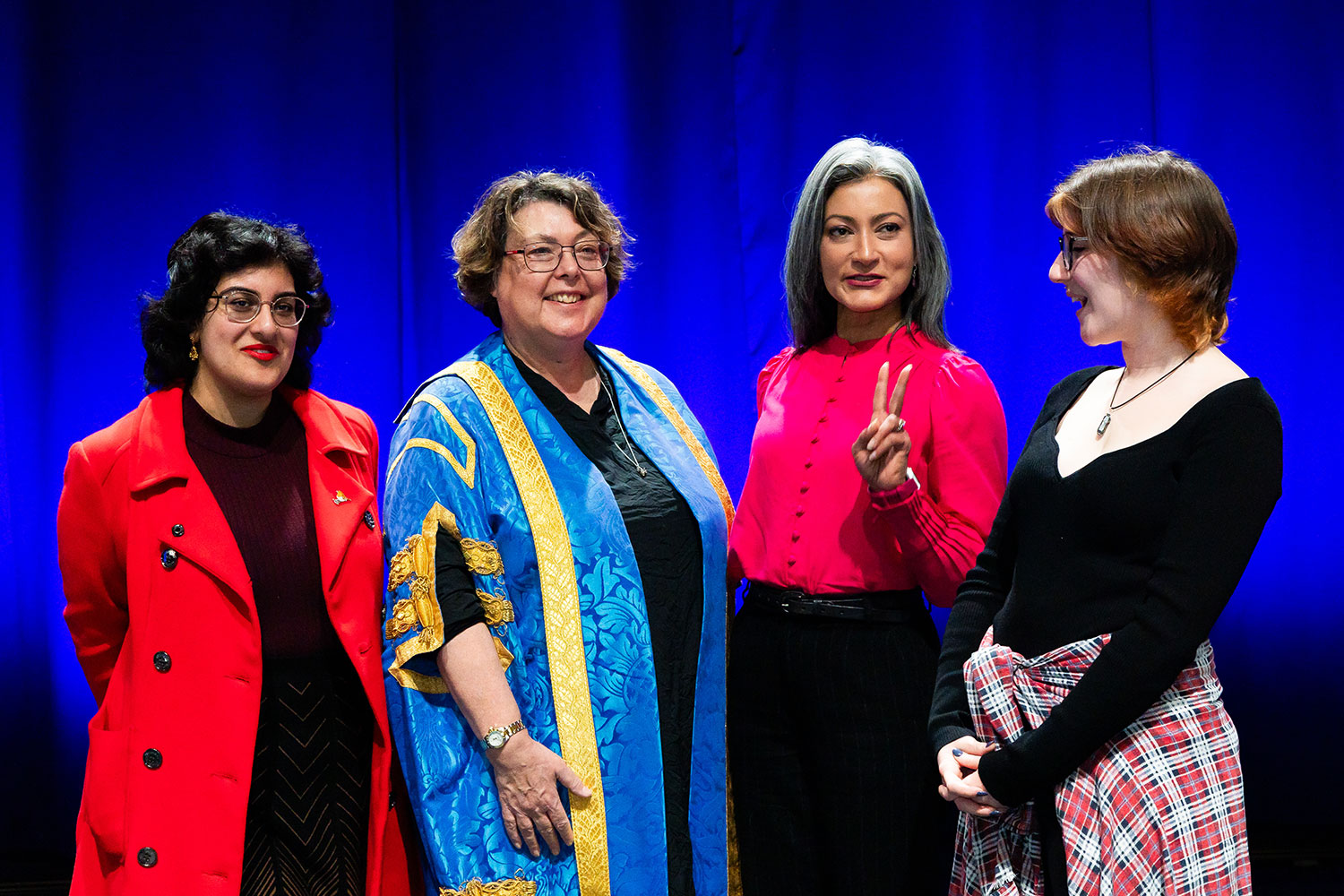 Sharanjit Leyl makes a peace sign on stage with Sue and staff from our Student Union