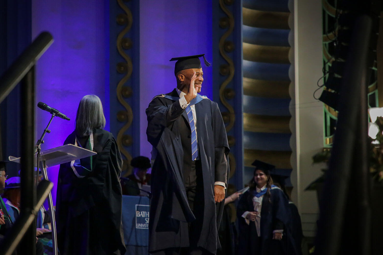 Graduand waves at the audience while crossing the stage at The Forum