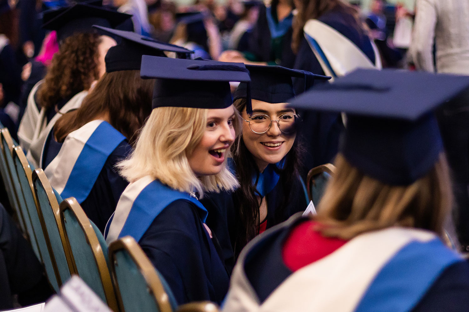 Graduands chatting excitedly to each other while sitting in the audience at a graduation ceremony