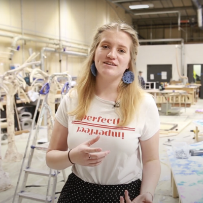 A student in a busy studio talks to the camera