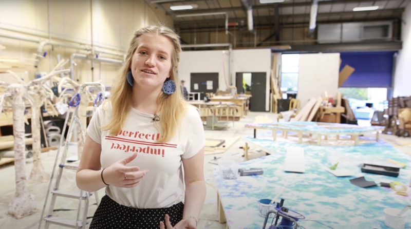 A student in a busy studio talks to the camera