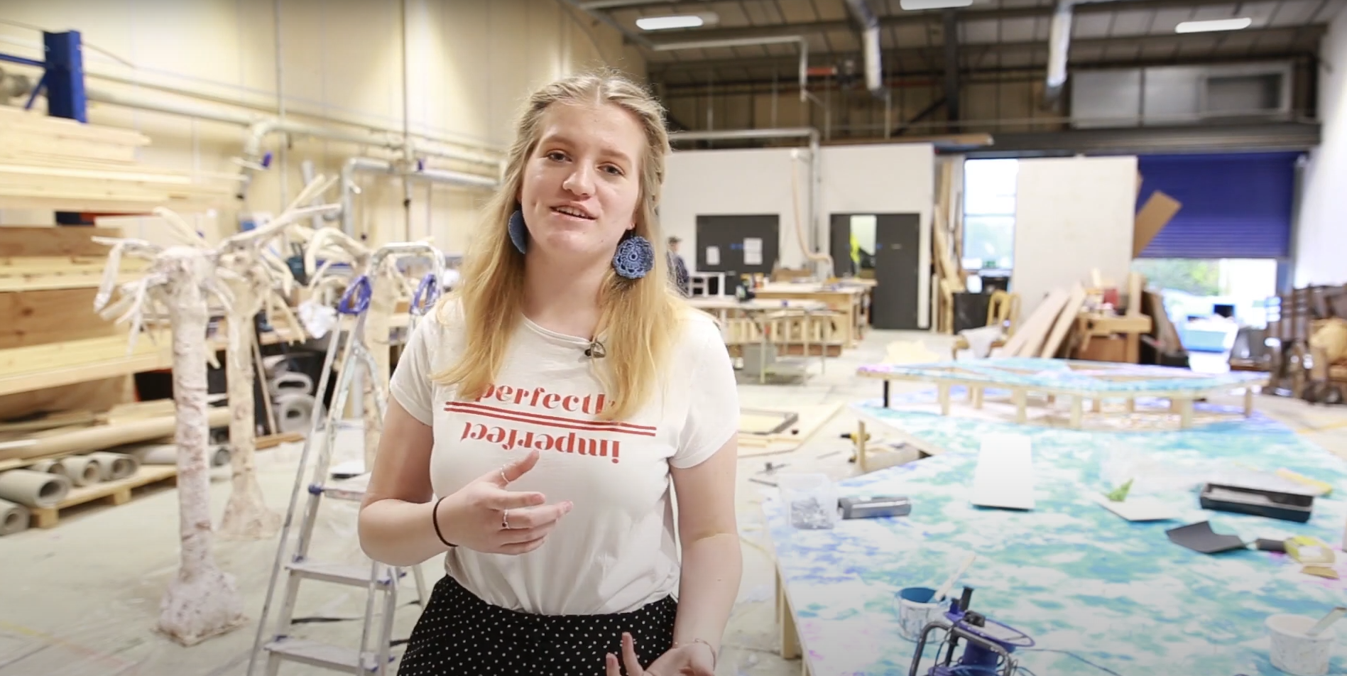A student in a busy studio talks to the camera