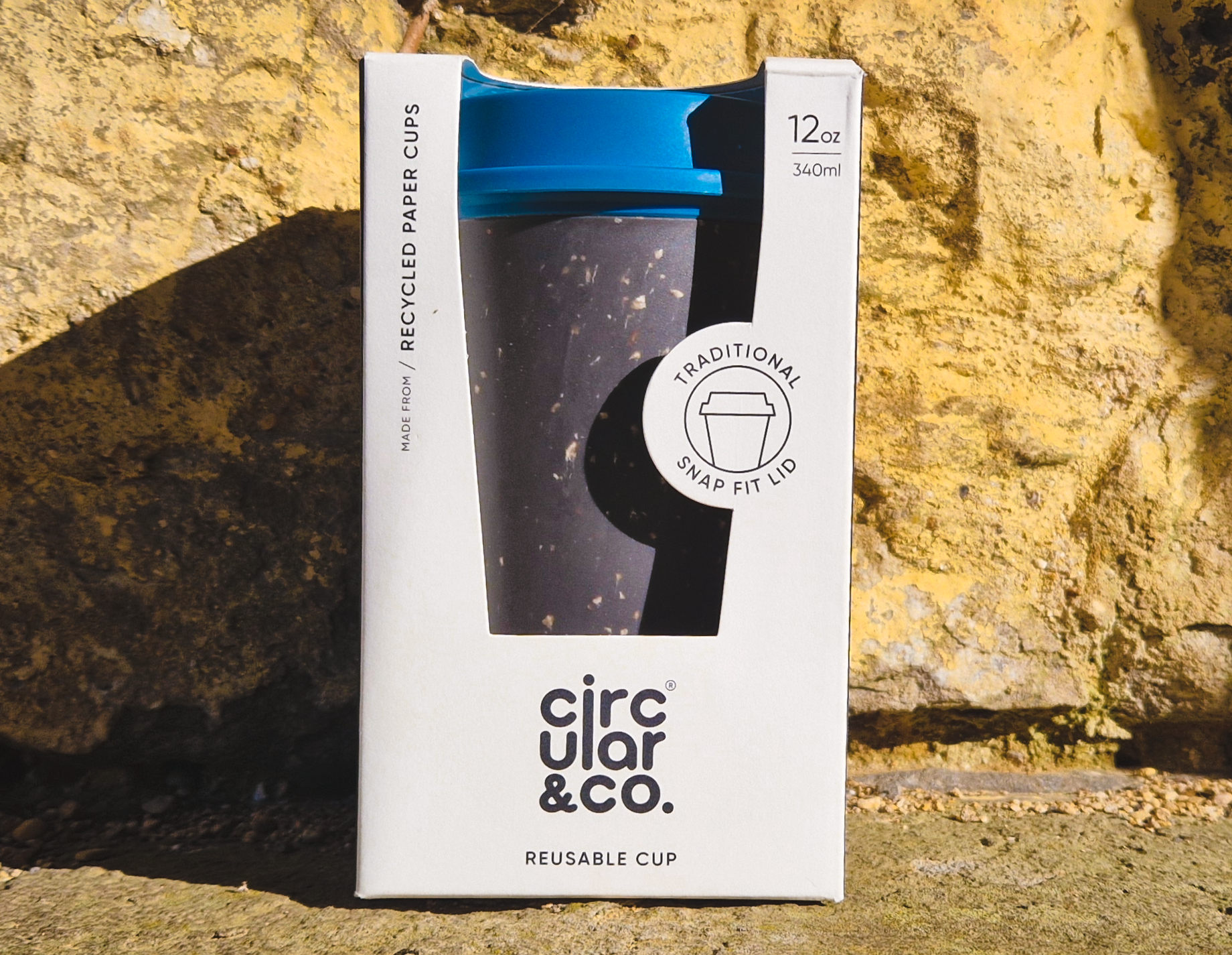 A black reusable coffee cup with a blue lid, packaged in a white box