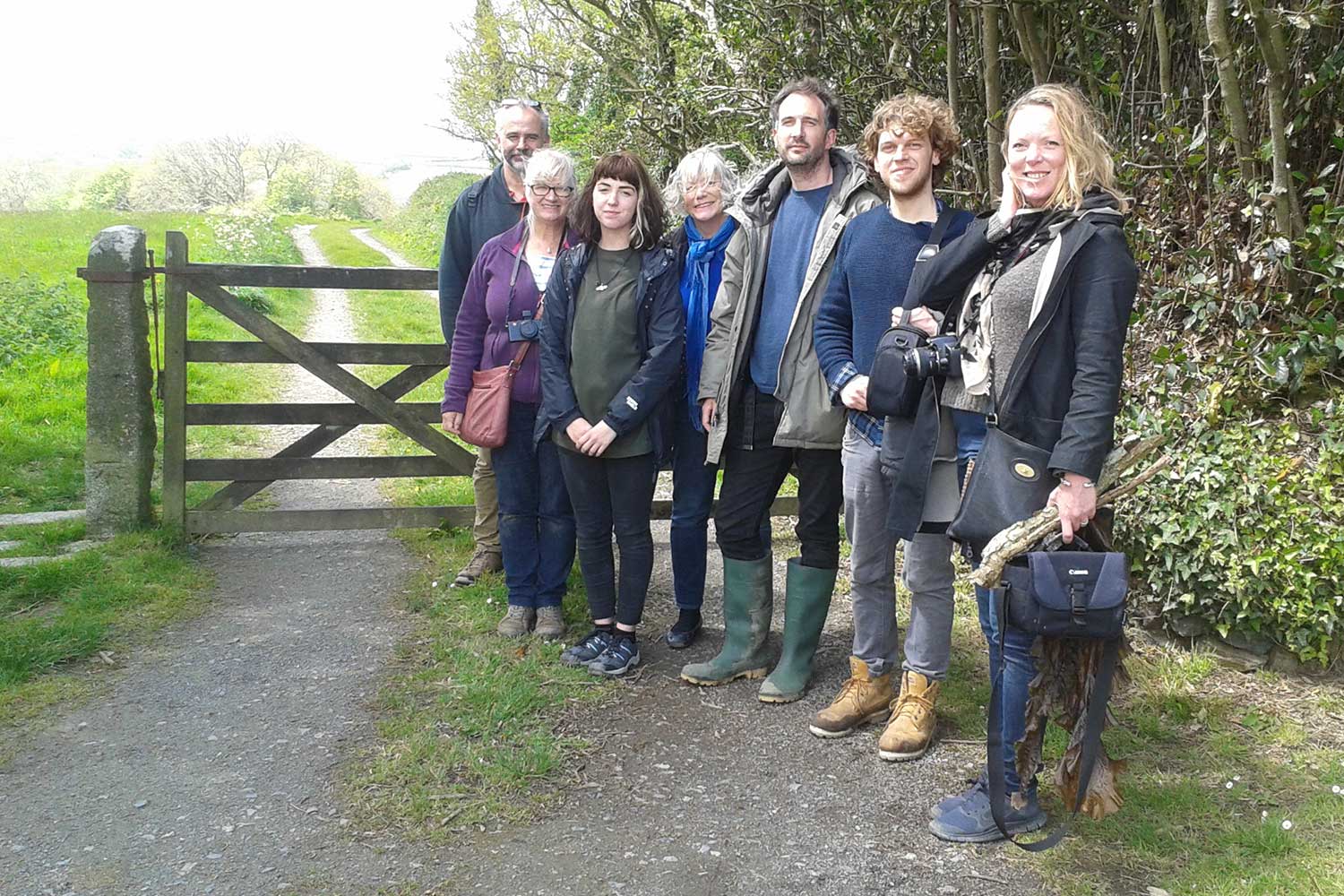 A group of people stand in front of a wooden gate in the countryside
