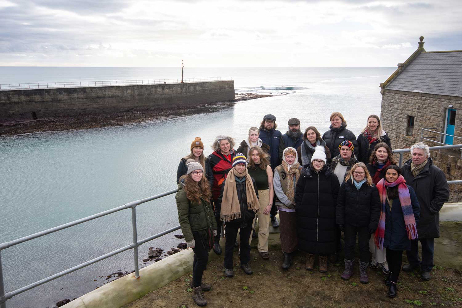 A group of people in winter clothing stand in front of Porthleven harbour