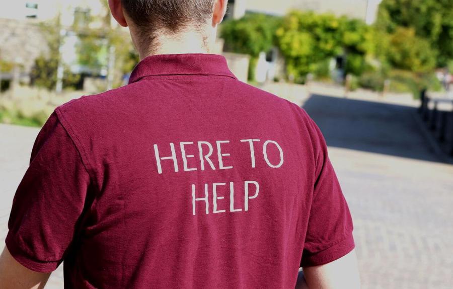 Back of a Bath Spa polo shirt that reads 'Here to help'