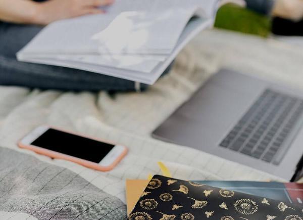 Student sitting outdoors on picnic blanket with books and laptop