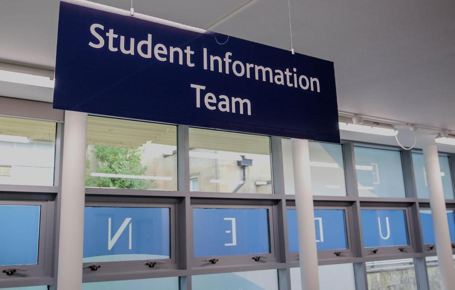 Large sign for Student Information Team hanging above a desk, with windows in the background.