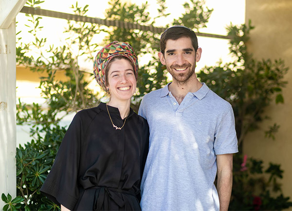 Two people arms round each other smiling in a leafy courtyard