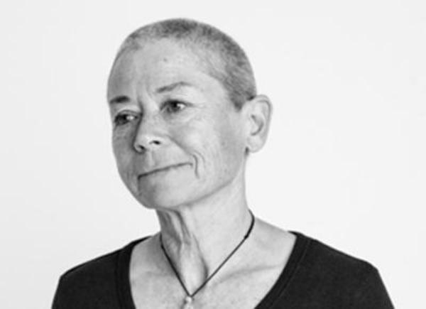 Person with very short hair wearing black top with pendant necklace