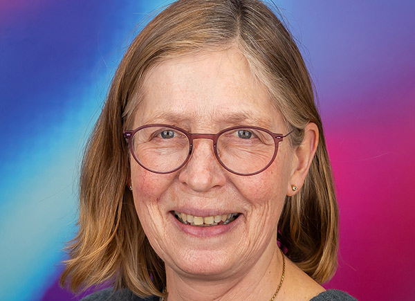 Headshot close up of someone with shoulder length light brown hair and glasses smiling