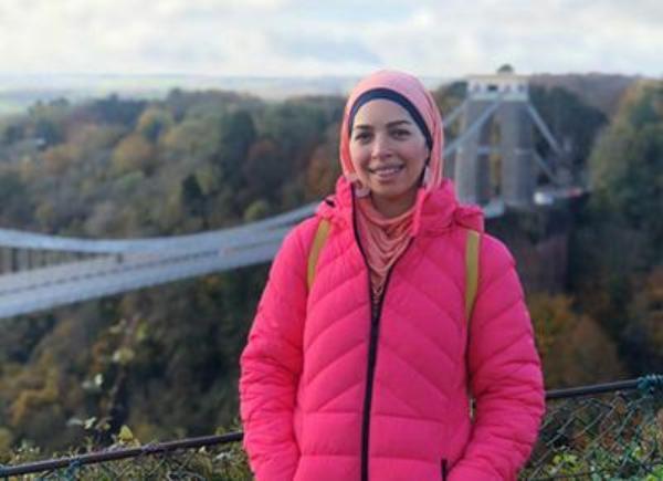 Person with headscarf and pink coat smiling in front of Clifton Suspension bridge