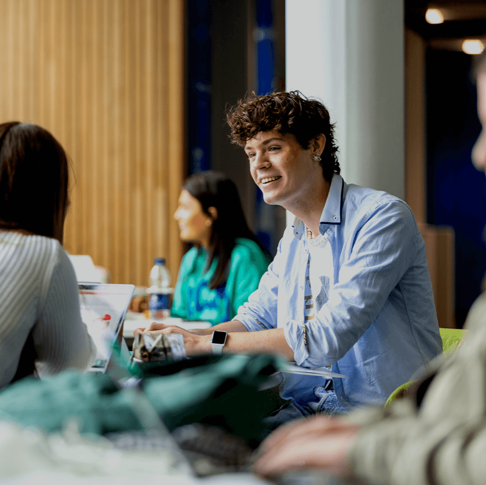 Three students around a table with laptops on it.