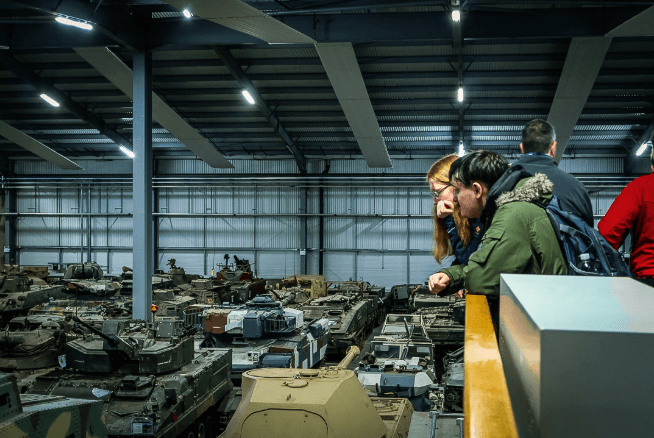 Two people look out over a large warehouse full of tanks.