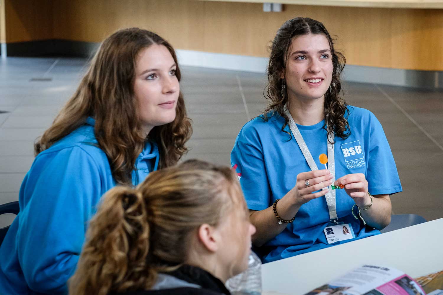Three student ambassadors smiling at person unseen in the Atrium NP
