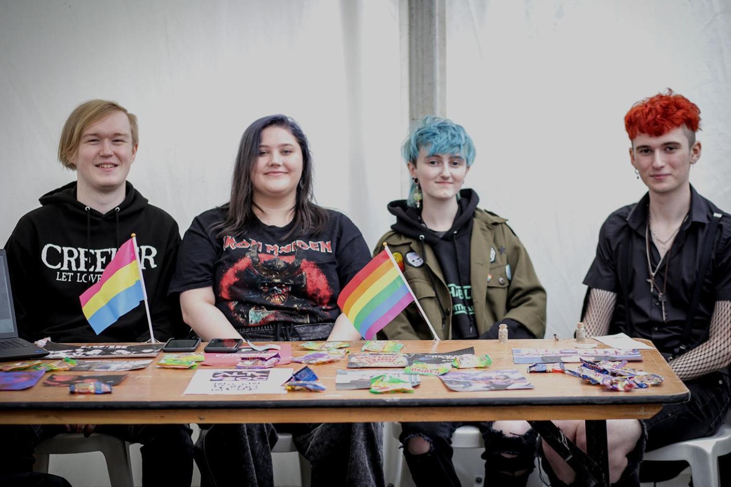 A group of students sit behind a trestle table covered in fliers and with a rainbow flag