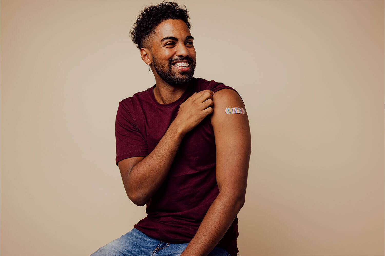 A male person of colour lifts his t-shirt sleeve to reveal a plaster where he has had a vaccination