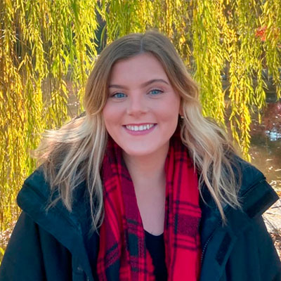 A woman with blonde hair and red checked scarf under a tree.