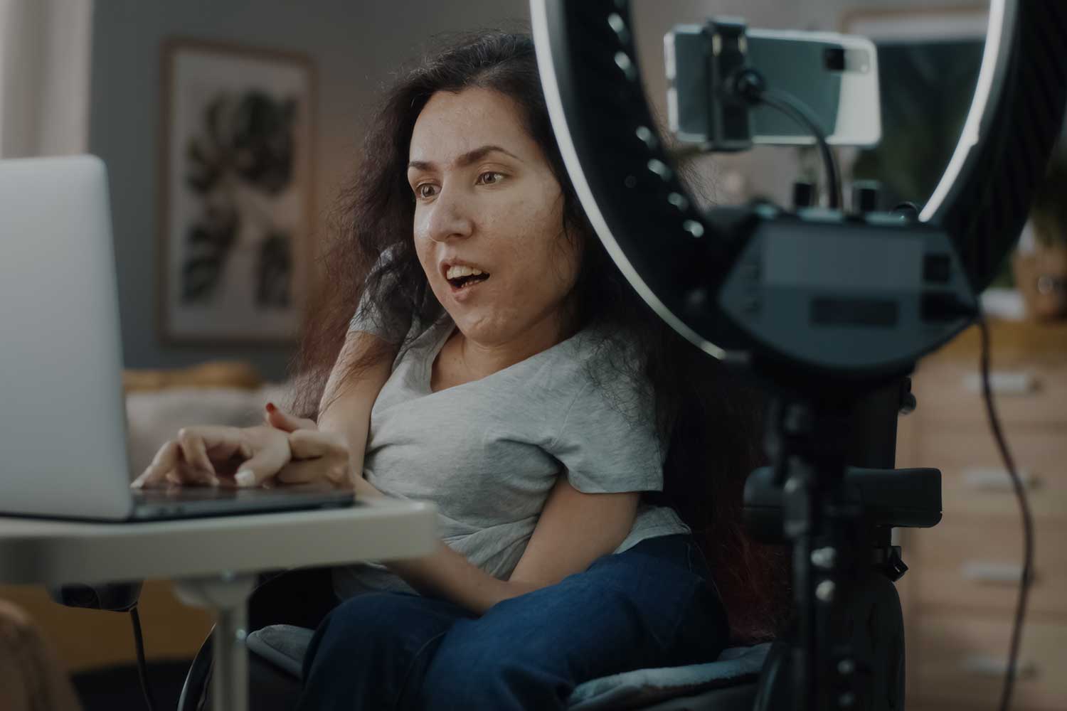An influencer positions her wheelchair in front of her camera, laptop and studio lighting